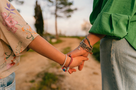 Close-up of two individuals holding hands, conveying a sense of connection and trust. The image captures a moment of togetherness, set on a picturesque outdoor pathwayの写真素材