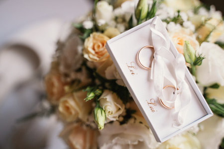 Close-up of two elegant wedding rings in a white box placed on a vibrant floral bouquet. The image captures the essence of love and commitment, perfect for wedding themes and romantic occasionsの写真素材