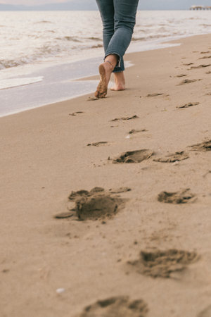 A serene moment captured as a person walks barefoot along the beach, leaving a trail of footprints...