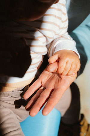 Child's hand gently holding an adult's open palm, capturing a moment of warmth and connection in sunlight. This tender interaction emphasizes affection and care across generationsの写真素材