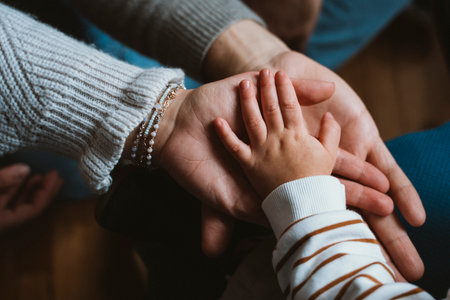 Warm image of hands showing adult, child, and baby hands stacked together. Emphasizes family unity,...