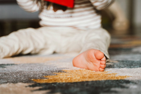 Child sitting on a soft, patterned carpet, focusing on a book in hand. Bare foot visible, suggesting relaxation and comfort during reading. Scene emphasizes cozy learningの写真素材