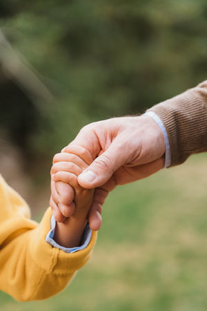 Close-up of an adult hand gently holding a child's hand, symbolizing connection, care, and support. The image captures a tender moment reflecting trust and securityの写真素材