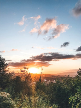 Golden sun setting behind a lush forest with distant mountains in view, casting a warm glow in the...