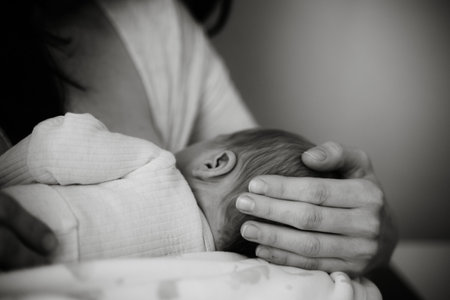 Mother gently breastfeeding her newborn, illustrating a serene moment of care and tenderness. The focus is on the nurturing bond and soothing environment during feedingの写真素材