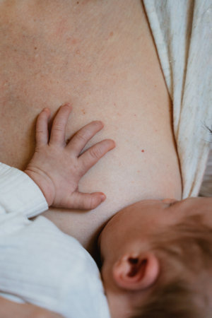 Mother gently breastfeeding her newborn, illustrating a serene moment of care and tenderness. The...