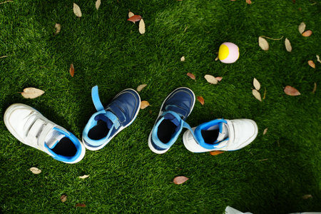 Children's sneakers scattered on green grass, accompanied by a small tennis ball. The image captures...