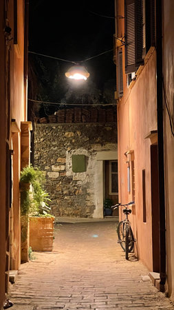 A serene nighttime alley scene features a vintage bicycle parked against a wall with an old lantern illuminating the path. Rustic stone and aged brickwork create a charming atmosphere.の写真素材