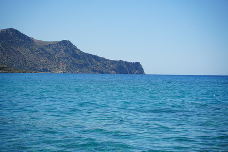 Dramatic coastline featuring azure blue waters with rugged rocky cliffs under a clear sky. The...