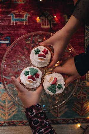 Three Christmas-themed cupcakes with Santa Claus and tree decorations held by children's hands on a...
