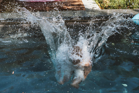 Water explodes into a dramatic splash as a person dives into the pool. The dynamic movement captures the joy and excitement of a summer day, with water droplets sparkling under the sun.の写真素材
