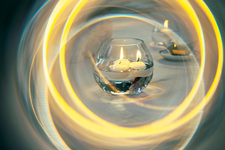 Floating candles softly glow inside a circular glass vase, surrounded by swirling patterns of yellow light. The serene scene creates a peaceful, intimate atmosphere perfect for relaxation.の写真素材