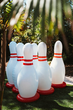 Inflatable bowling pins arranged on grass in a sunny outdoor environment. Surrounded by lush...