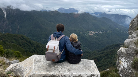 Father and daughter sit side-by-side on a stone ledge, gazing at stunning mountain vistas. The father embraces his daughter, capturing a moment of connection and tranquility.の写真素材