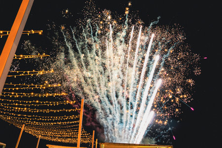 Stunning fireworks lighting up the night sky with bright sparks and vibrant colors, set against a backdrop of decorative strings of lights, creating a festive atmosphereの写真素材