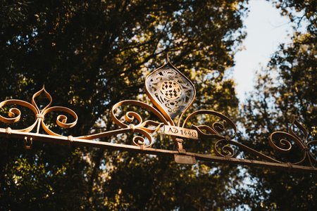 Vintage iron gate with ornate designs and an inscription marked AD 1448. The intricate metalwork highlights historical craftsmanship against a backdrop of dense forest trees.の写真素材