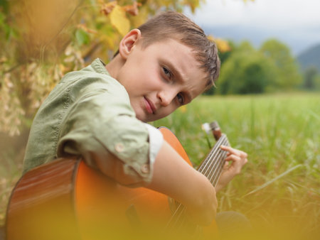Young Boy Playing Guitar Outdoors in Natureの写真素材