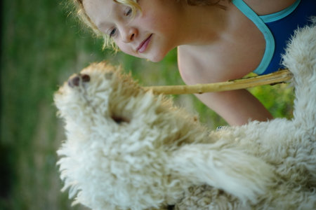 Child and fluffy dog enjoy a playful moment outdoors. The child holds a stick, and both share a joyful connection. This candid scene captures youthful innocence and pet companionship.の写真素材