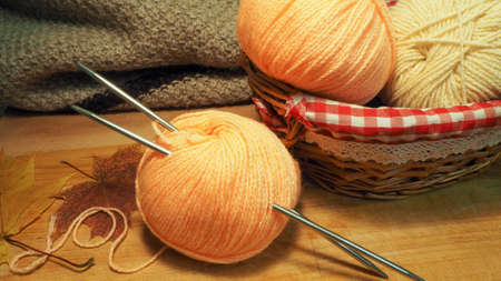 A skein of woolen threads and knitting needles on the background of a basket with balls and a...