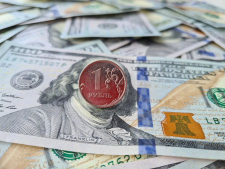 Coin with a face value of 1 ruble against the background of a banknote with face value of 100 dollars closeup. On coin is an inscription in Russian letters ruble.の写真素材