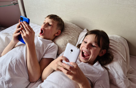 Surprised shocked kids with mobile phone play online games. Emotions of delight and Internet use in childhoodの写真素材