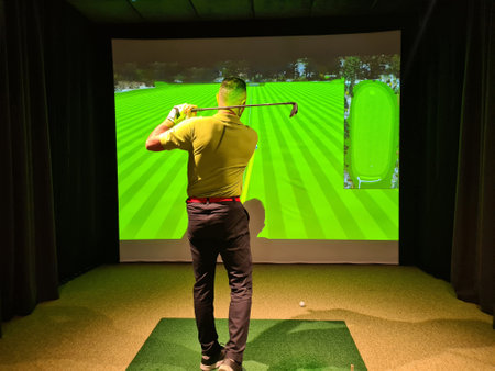 Man playing golf on screen and golf simulator. Young golfer playing golf video game indoorsの写真素材