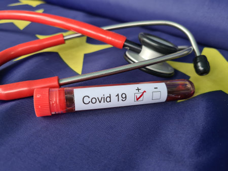 Stethoscope and test tube with positive blood sample against background of European Union flag. Coronavirus outbreak covid-19の写真素材