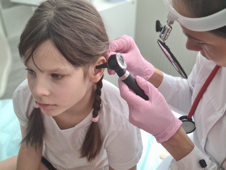 Female doctor conducts medical examination of inflamed ear with otoscope to little girl. Hearing test for childrenの写真素材