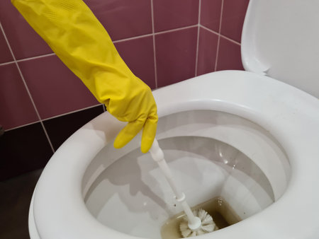 Woman in rubber glove cleans toilet with brush. Dirty toilet plumbing and cleaning conceptの写真素材