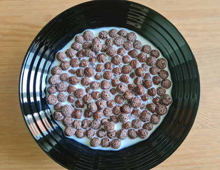 Chocolate corn flakes with milk. Chocolate breakfast cereal in a white bowl on a wooden table. top...