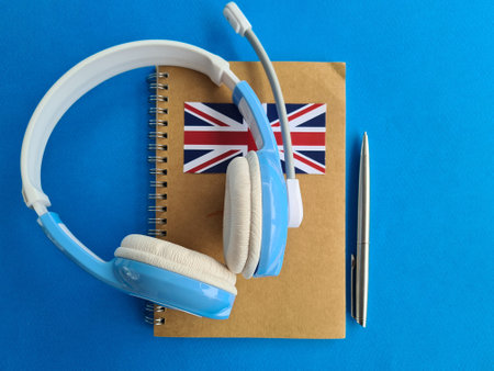 Notepad with British flag pen and headphones on blue background. English language learning and audio courses conceptの写真素材