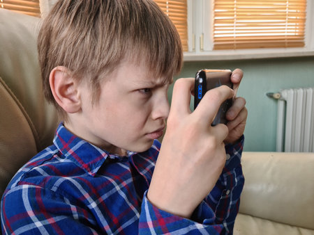 Teenager child with poor eyesight squints and looks at screen. Hyperopia myopia astigmatism glaucoma and addiction to gadgetsの写真素材