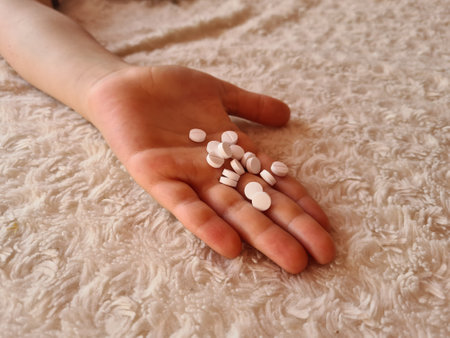 Girl child took large doses of pills and lies on bed. Indifferent child holding several pills in handsの写真素材