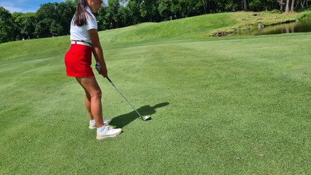 Woman holds golf club behind back. Rear view of a woman playing golf on a green lawnの写真素材
