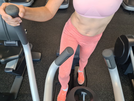 Female legs exercising on elliptical machine in gym. Sports fitness health