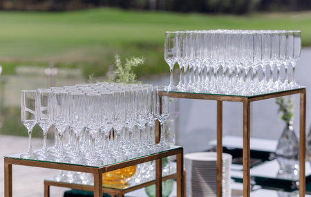 Elegant champagne flutes arranged on tables for an outdoor celebration near a lush green landscape in bright daylightの写真素材