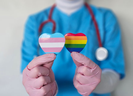 Healthcare worker holding transgender and rainbow pride symbols while advocating for inclusivity in medicineの写真素材