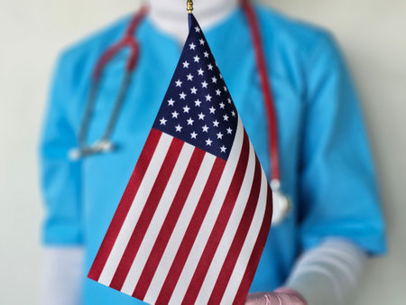Healthcare professional holding a small American flag while wearing scrubs in a clinical settingの写真素材