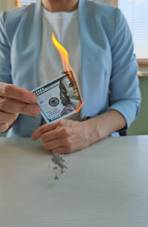 One hundred dollars are burning with fire in the hand of businesswoman. Economic monetary inflation and bankruptcyの写真素材