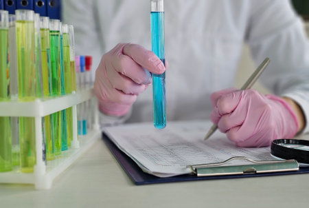 A laboratory technician in gloves holds a blue test tube and notes data on a clipboard. Colorful...