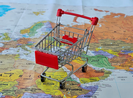 Small shopping cart on a pile of cash placed over a world map representing global commerce and financeの写真素材