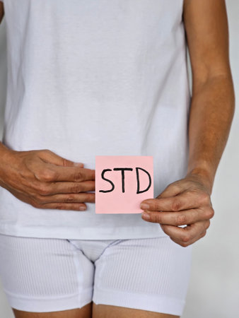 Woman holds paper with STD inscription. Female person feels symptoms and pain due to sexually transmitted diseasesの写真素材