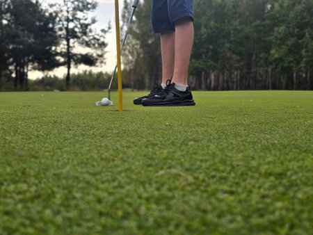 A golfer prepares to putt on the green at a forested golf course during late afternoonの写真素材