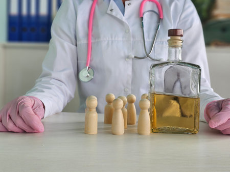 A medical professional in a white lab coat examines a group of wooden figures next to a bottle of clear liquid in a healthcare settingの写真素材