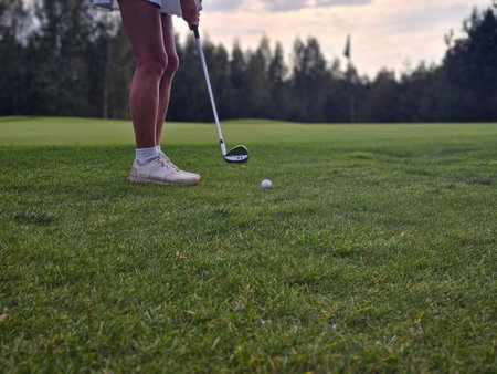 A golfer prepares to swing at a ball on the green during golden hour at a tranquil golf courseの写真素材