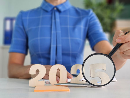 A woman examines the number 2025 through a magnifying glass while planning ahead at an office deskの写真素材