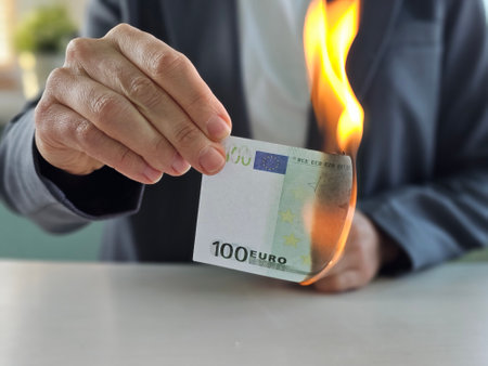 Person holding a burning 100 euro banknote in a modern indoor setting during daylightの写真素材