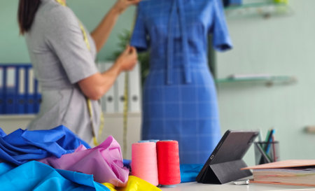 Tailor measures garment on dress form in a bright creative workspace with colorful fabrics and toolsの写真素材