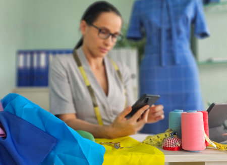 A focused seamstress uses her smartphone while surrounded by vibrant textiles, sewing accessories...