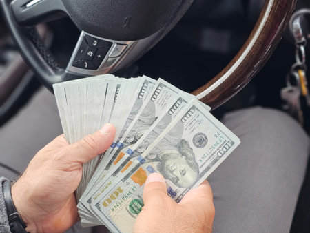 Individual counting cash in a car during the day while seated in the driver seat